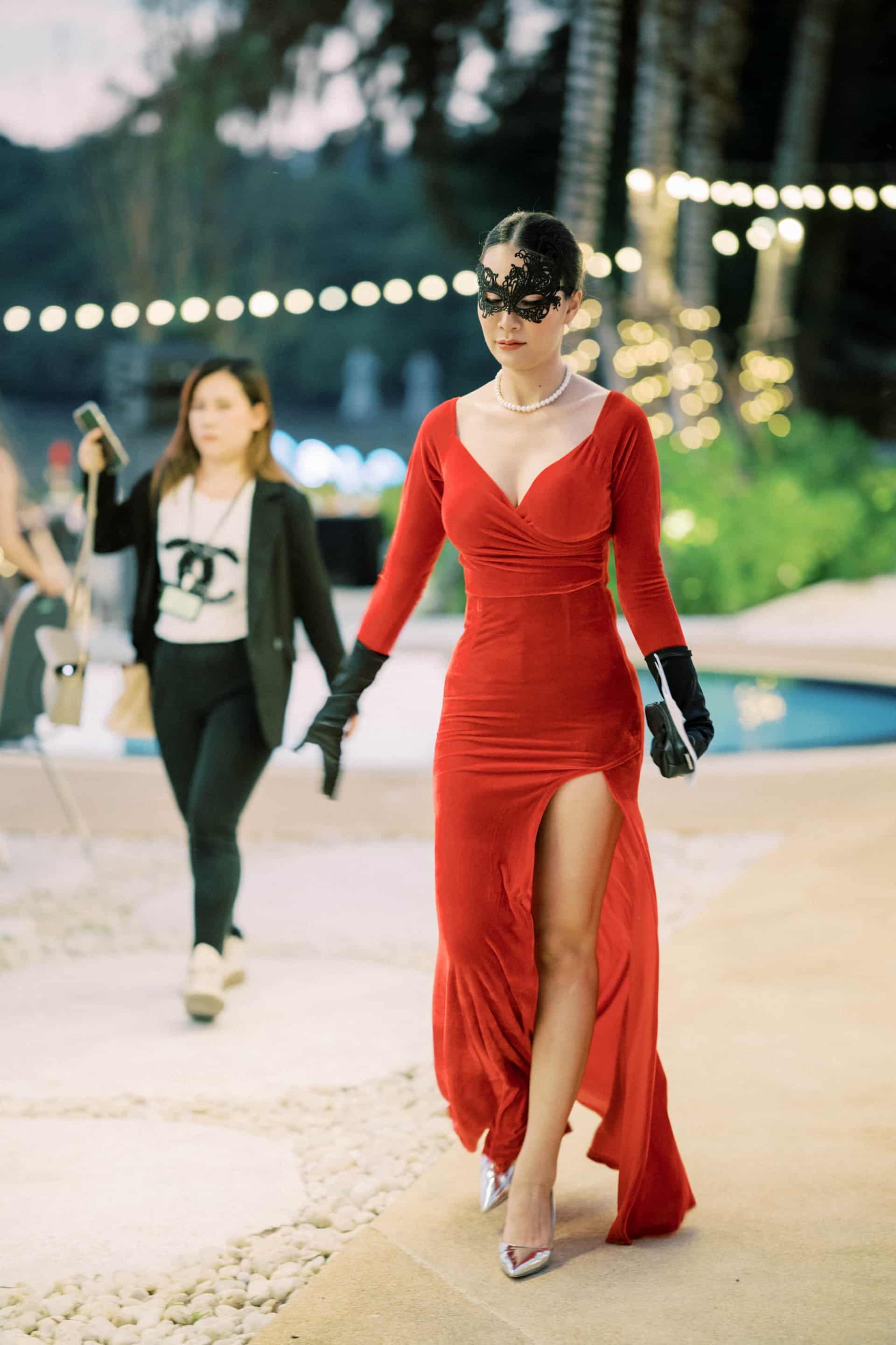 Parties And Events3 A woman in a red dress and mask strolls by a serene pool, embodying elegance at a gala dinner in Phuket event venues.